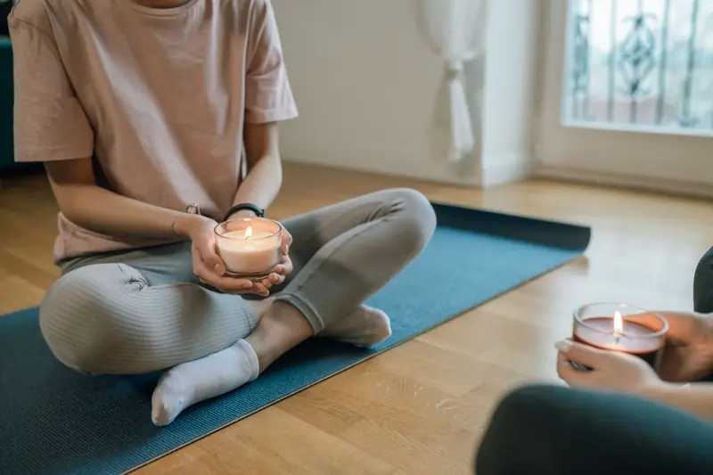 Woman holding a candle seated for meditation on yoga mat indoors