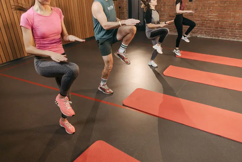 A group performs high knees together in an indoor fitness studio with yoga mats