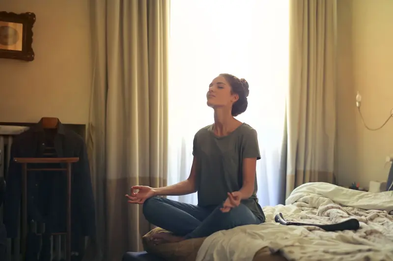 Adult woman practicing meditation on her bed surrounded by a calm bedroom atmosphere