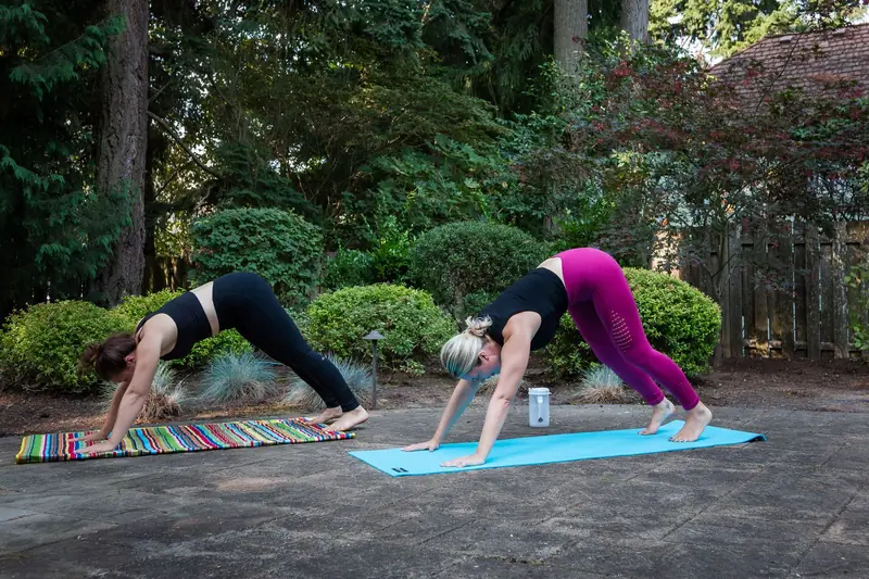Two women perform yoga exercises on mats in a serene outdoor setting