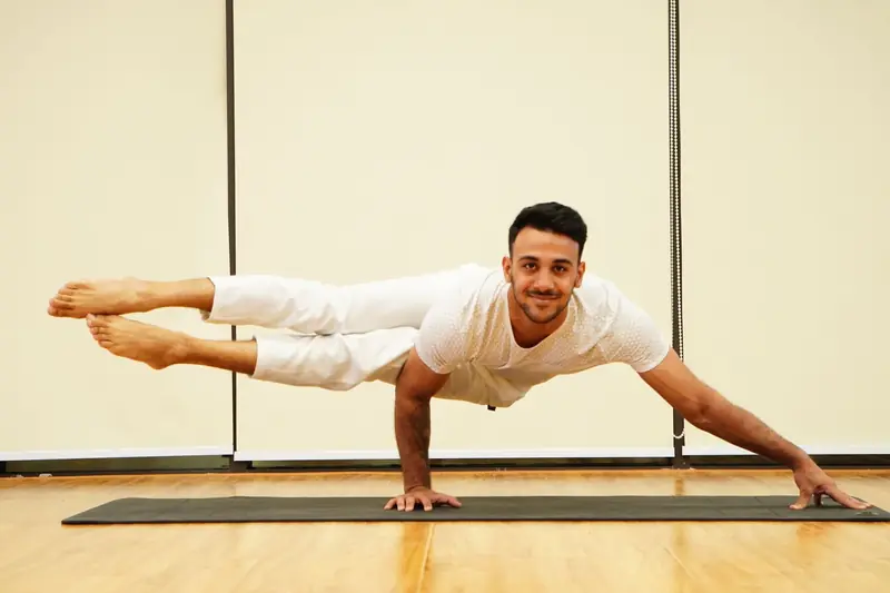 A man balances in an advanced yoga pose on a mat indoors, showcasing strength and focus