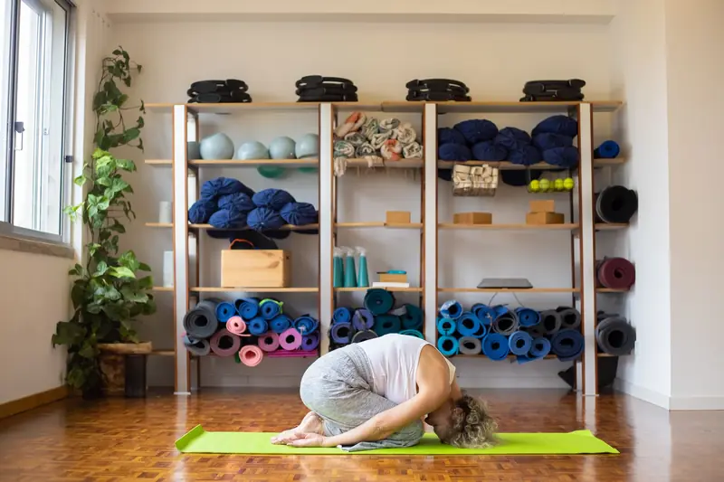 A woman performs yoga on a mat in a well-equipped studio, surrounded by props and natural light