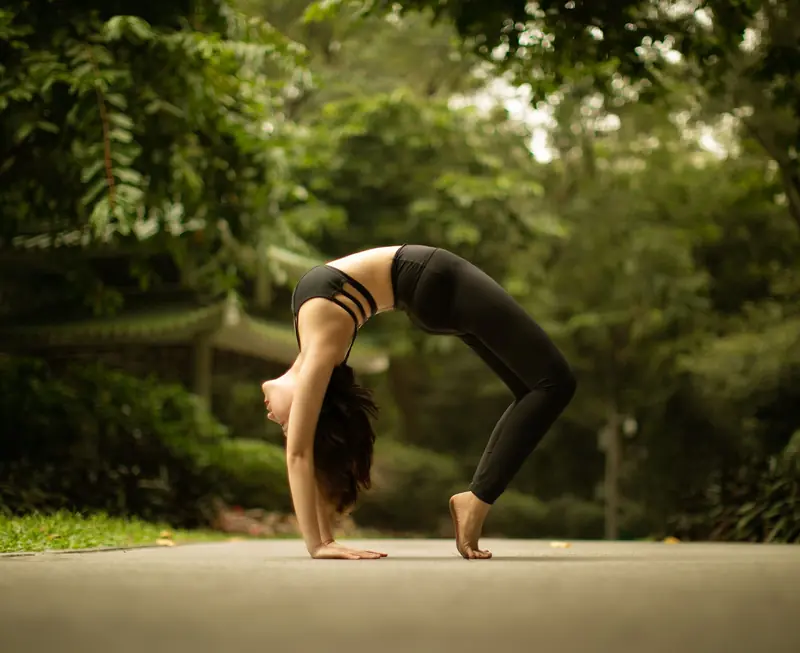 Woman performing yoga wheel pose in a peaceful outdoor park. Fitness and mindfulness in nature
