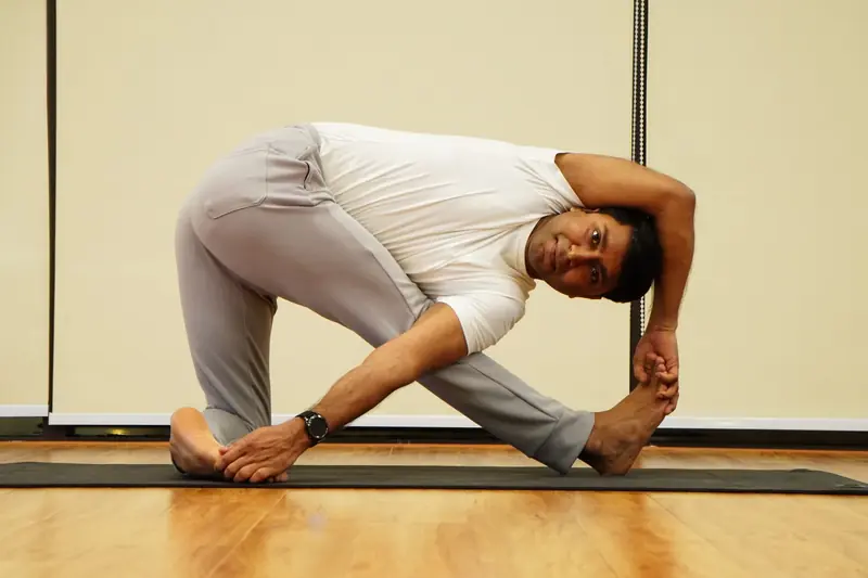 Man performing an advanced yoga stretch indoors on a yoga mat, showcasing flexibility and strength