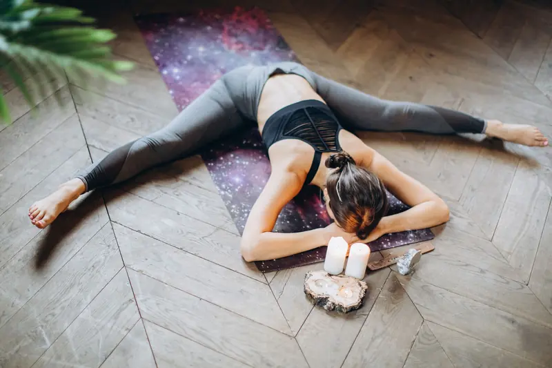 Woman in yoga pose indoors with candles and yoga mat, promoting relaxation and mindfulness