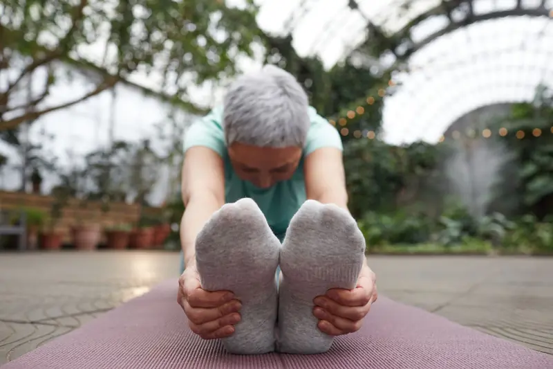 A senior woman with gray hair performs a yoga forward fold indoors, embracing mindfulness and tranquility