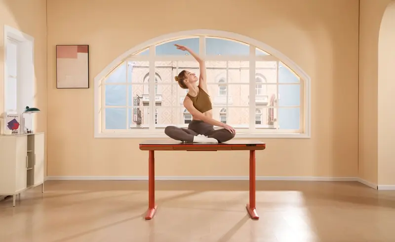 Woman practicing yoga on a desk in a bright, modern office with a large window