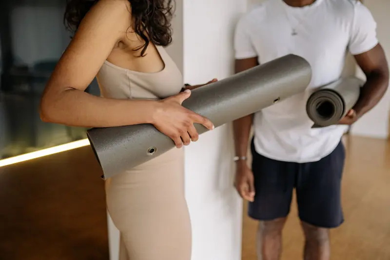 Two adults holding yoga mats in a studio, promoting fitness and wellness