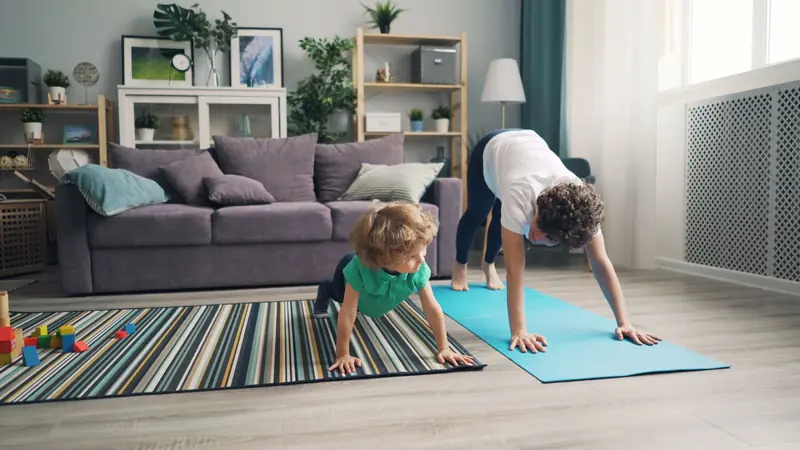 A mother and her child practice yoga together in a cozy living room setting. Family fitness at home
