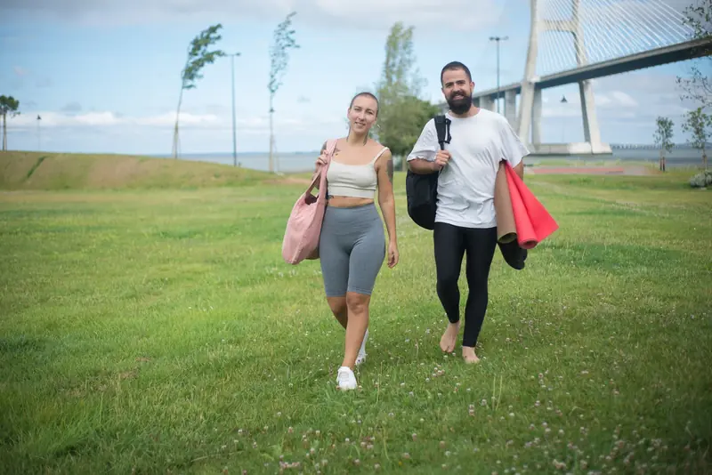 Couple walking in Lisbon park with yoga mats, showcasing active lifestyle in natural setting