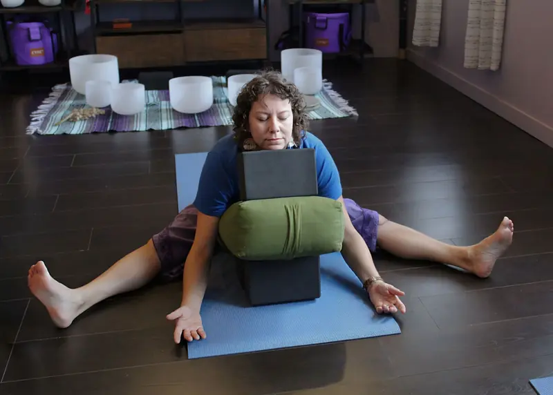 A woman practicing restorative yoga indoors using blocks and cushions for support