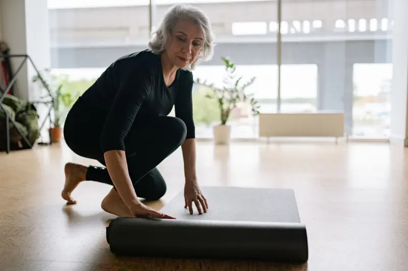 Senior woman setting up yoga mat in bright studio, preparing for exercise