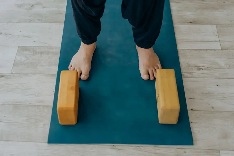 Close-up of feet on a yoga mat beside wooden blocks indoors