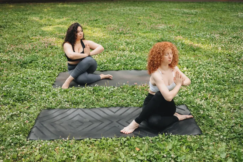 Two women practicing yoga in a tranquil outdoor setting, surrounded by lush grass