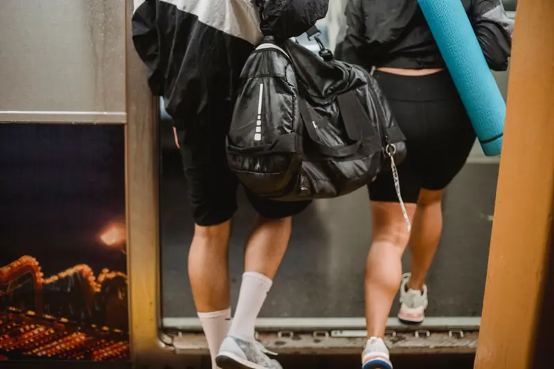 A man and woman boarding a subway train carrying a duffle bag and yoga mat, dressed in athletic gear