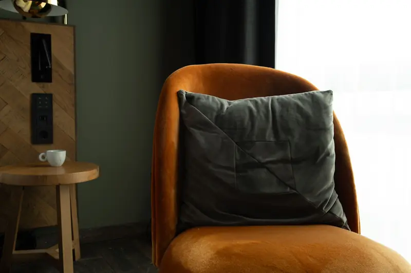 A warm, inviting corner with an orange velvet chair, grey cushion, and a small coffee table in a modern interior setting