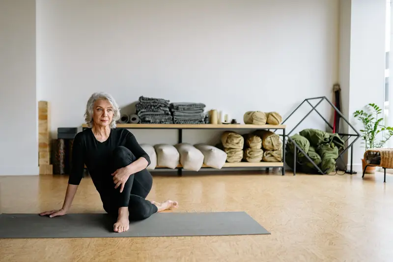 Elderly woman performing yoga exercise indoors on a mat, in a calm and serene setting