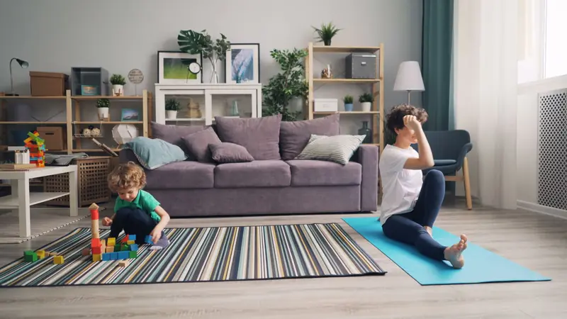 A mother practicing yoga and her child playing with blocks in a cozy living room
